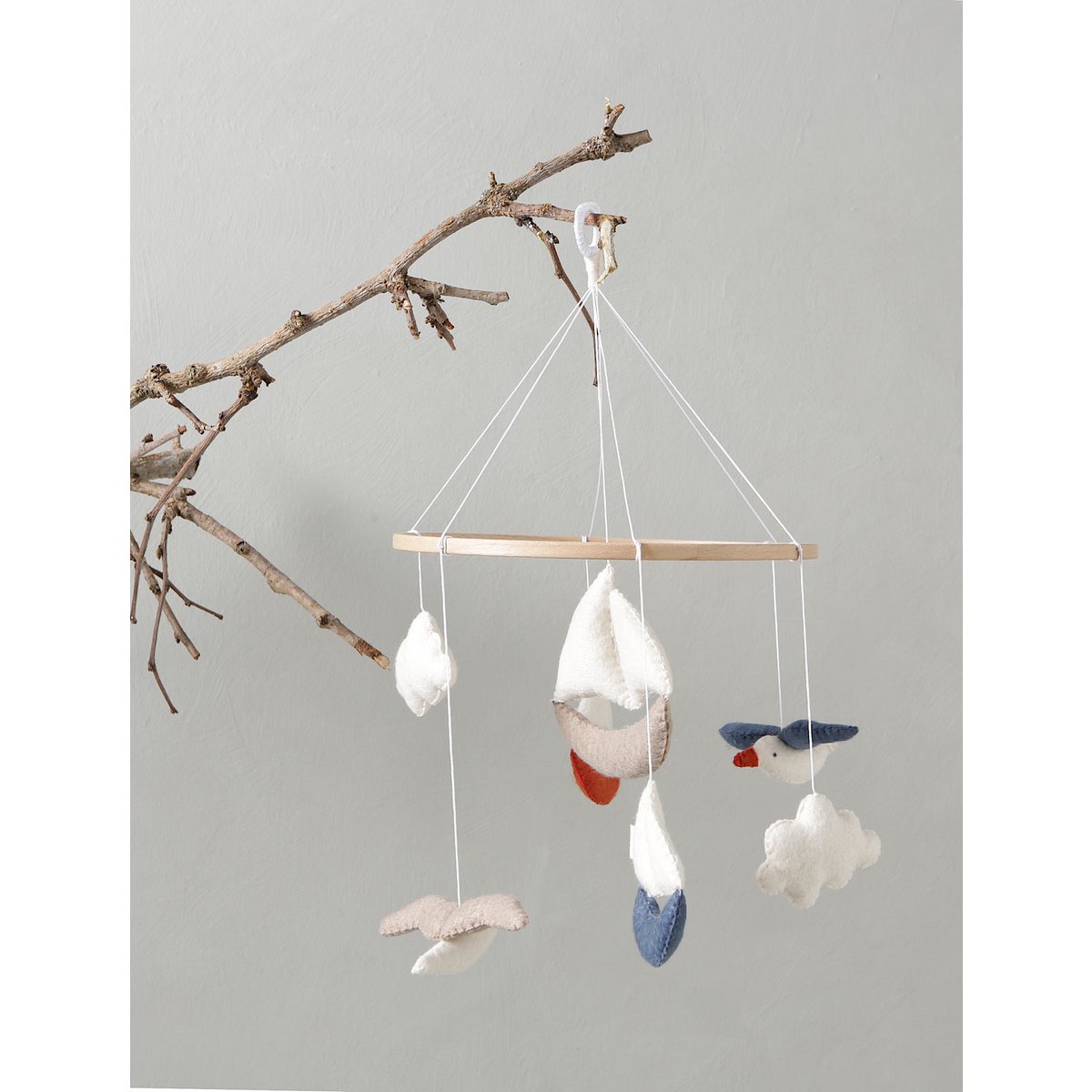 MARINA Mobile von 2 Stories, hängend an einem naturbelassenen Ast – mit handgefertigten Filzfiguren wie Booten, Möwen und Wolken in Weiß, Blau, Rot und Beige.