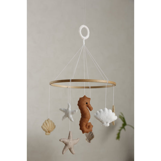 Filz-Mobile SEA von 2 Stories aus Holz in Weiß und Beige: In der Mitte hängt ein Seepferdchen, umringt von drei Muscheln und drei Sternen – maritimes Design für das Babybett.