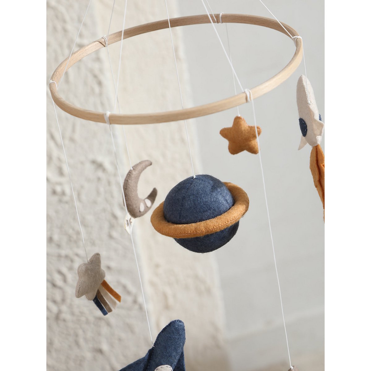 SPACE Baby-Mobile von 2 Stories aus Filz und Holz – mit zwei Raketen (blau und weiß) mit Feuerschweif, einem blauen Saturn in der Mitte, einem weißen Stern mit Schweif, grauem Mond sowie einem gelben und einem weißen Stern – in sanften Beige-, Blau- und Grautönen.