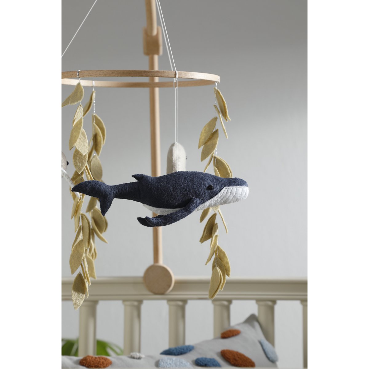 Filz-Wal aus dem OCEAN Mobile von 2 Stories vor einem Babybett – in sanften Blau- und Grautönen, handgearbeitet und liebevoll gestaltet