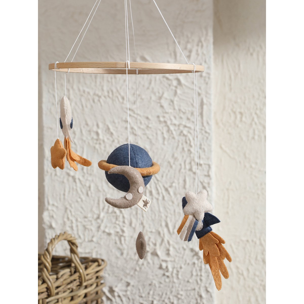 Detailaufnahme vom SPACE Baby-Mobile: blaue Rakete mit Feuerschweif, weißer Stern mit Schweif und grauer Mond – aus Filz gefertigt und hängend an einem Holzrahmen