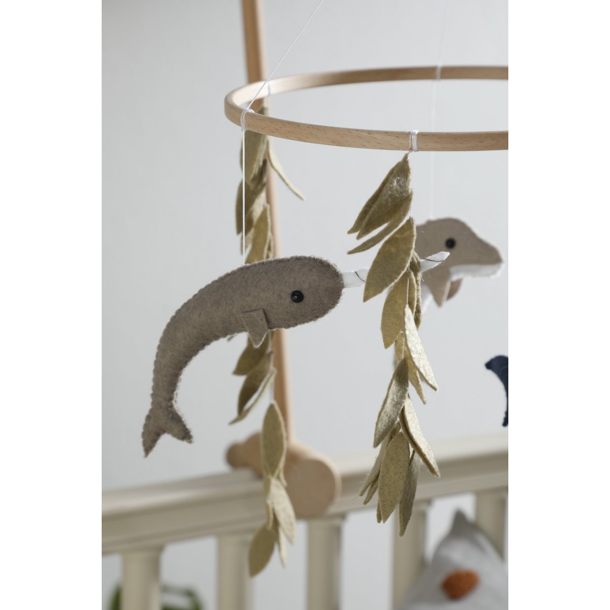 Schwertfisch aus Filz mit grünen Algen vor einem weißen Bettgitter – Teil des handgefertigten OCEAN Mobiles von 2 Stories.