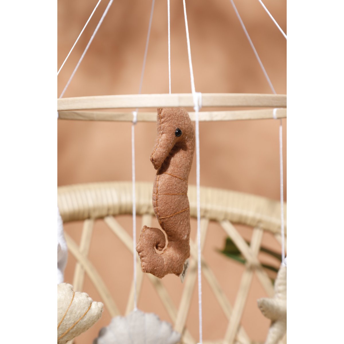 Detailansicht eines handgefertigten Seepferdchens aus Filz – cremeweiß mit filigranen Nähten und sanft geschwungener Form, zentrales Element des SEA Mobiles von 2 Stories.