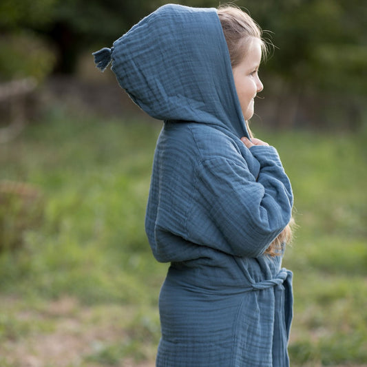 Kind steht in der Natur und trägt den Baby-Bademantel aus Bio-Musselin, indigo blau