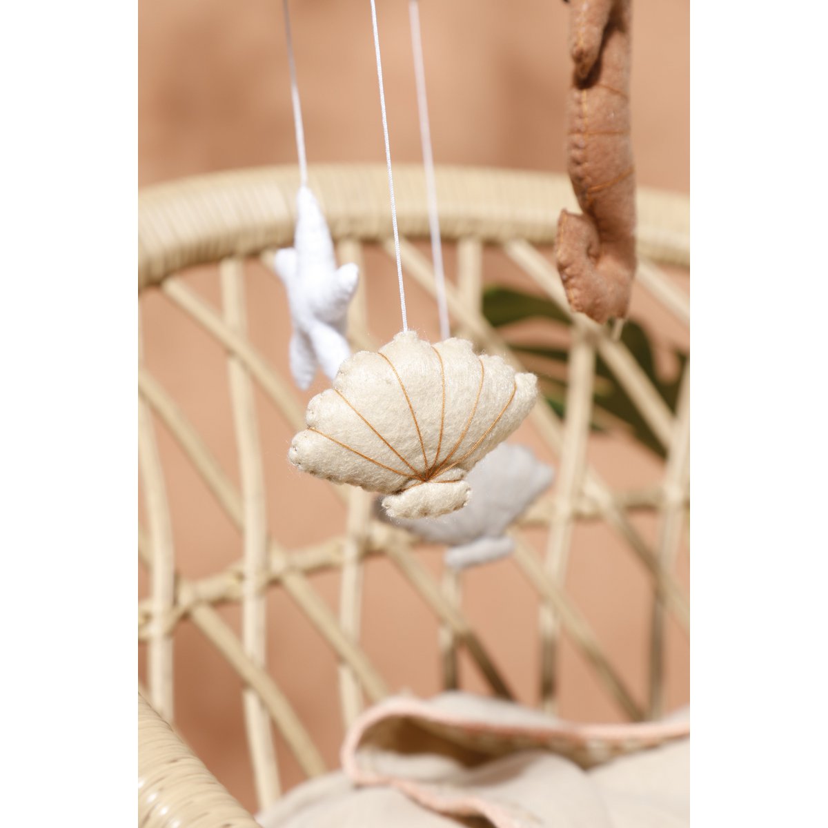 Nahaufnahme einer handgefertigten, beigefarbenen Filzmuschel aus dem SEA Mobile von 2 Stories – zarte Wollstruktur, sanft geschwungene Form.