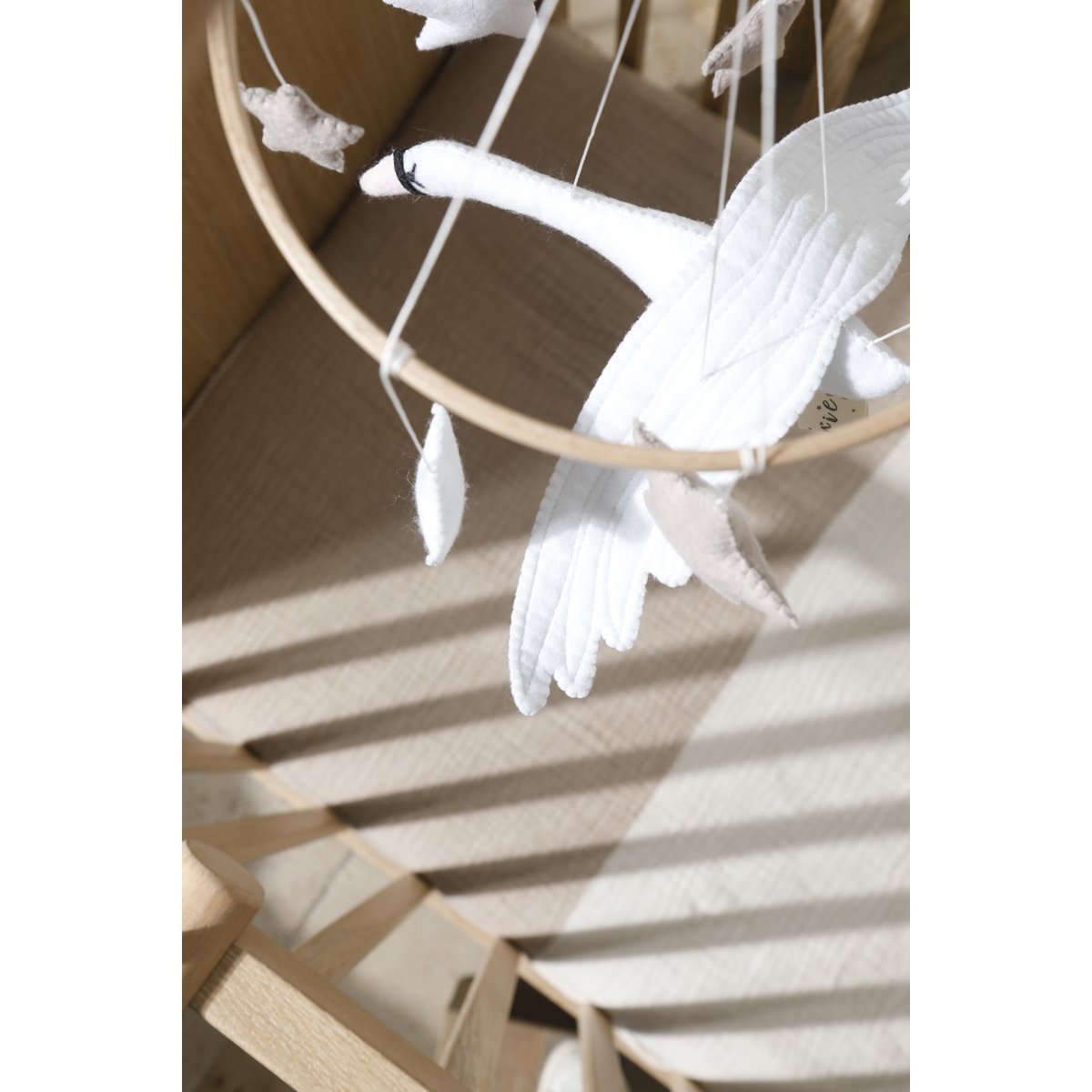 Blick von oben auf das SWAN Mobile aus Filz: ein weißer Schwan mit sieben dekorativen Sternen in Weiß, Beige und Bronze – liebevolle Handarbeit für das Babybett.“