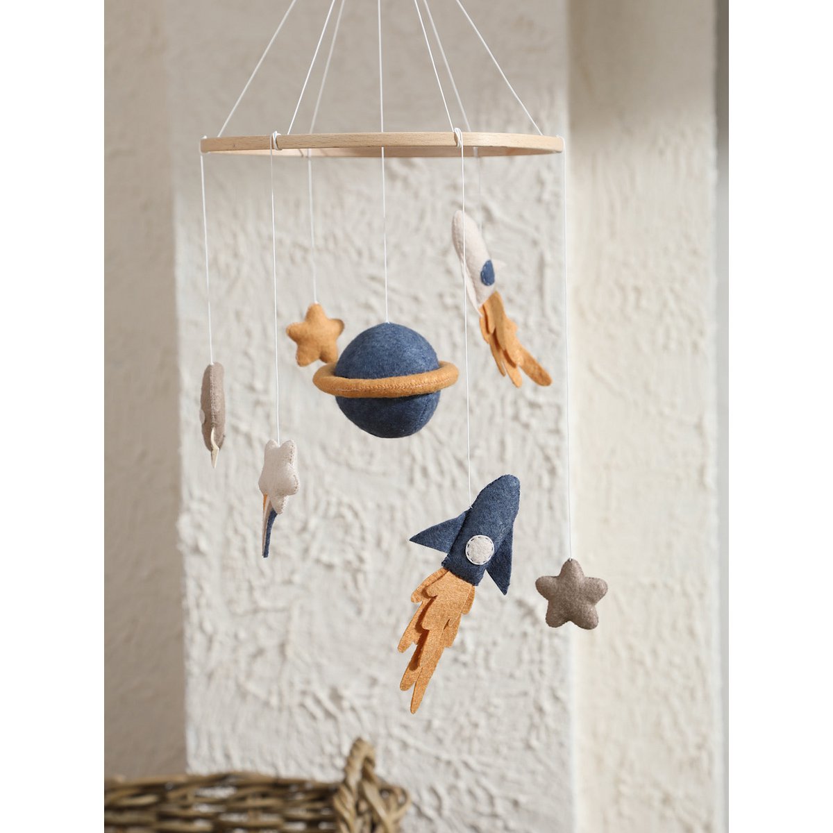 SPACE Baby-Mobile von 2 Stories aus Filz und Holz – mit zwei Raketen (blau und weiß) mit Feuerschweif, einem blauen Saturn in der Mitte, einem weißen Stern mit Schweif, grauem Mond sowie einem gelben und einem weißen Stern – in sanften Beige-, Blau- und Grautönen.