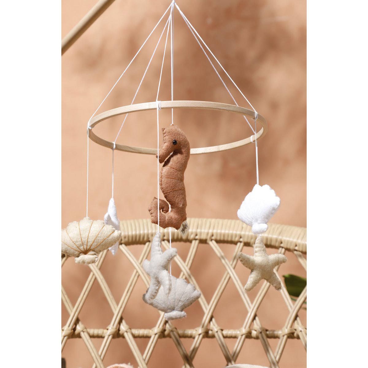 Filz-Mobile SEA von 2 Stories aus Holz in Weiß und Beige: In der Mitte hängt ein Seepferdchen, umringt von drei Muscheln und drei Sternen – maritimes Design für das Babybett.