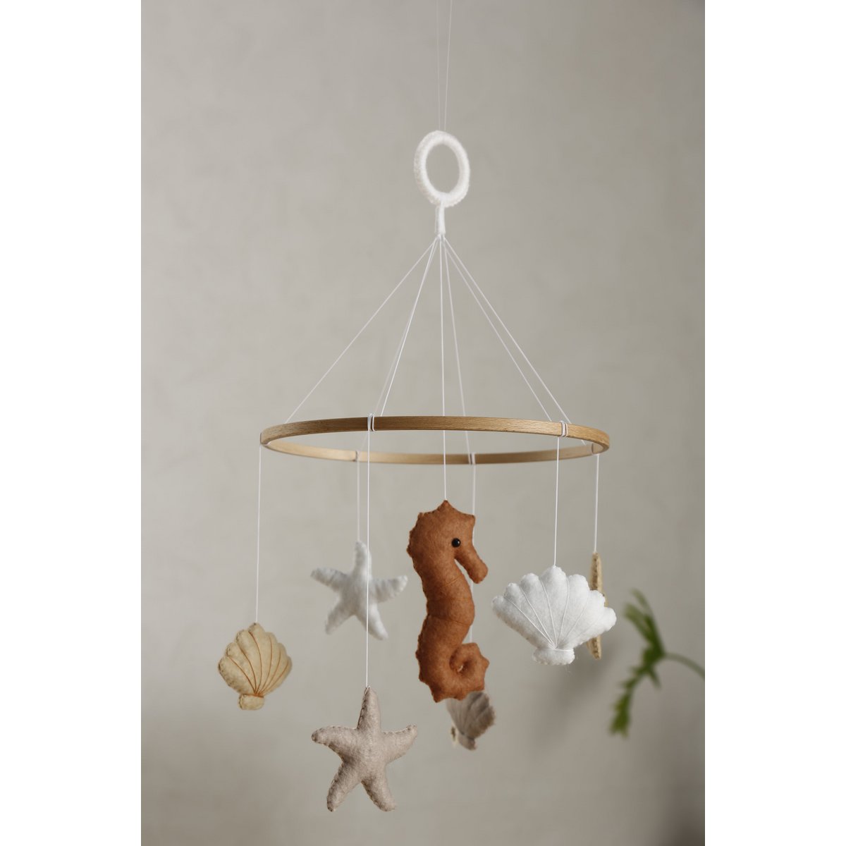 Filz-Mobile SEA von 2 Stories aus Holz in Weiß und Beige: In der Mitte hängt ein Seepferdchen, umringt von drei Muscheln und drei Sternen – maritimes Design für das Babybett.