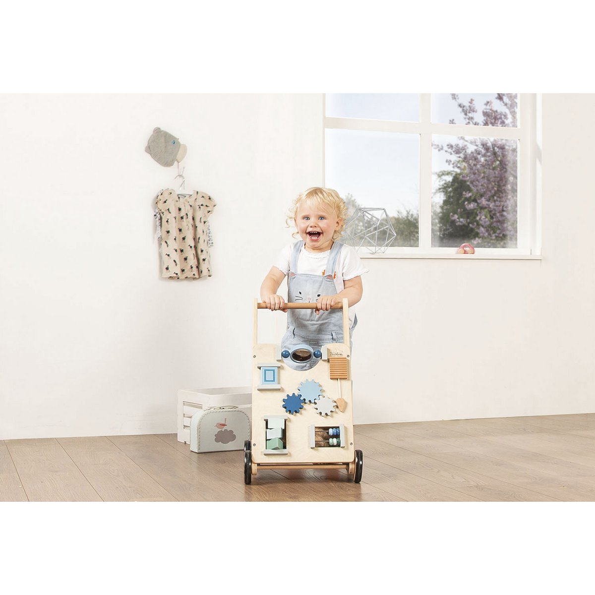 Lachendes Kind läuft und schiebt Activity Walker 'Titus' in Blau, Holzspielzeug mit interaktiven Elementen, unterstützt das Laufenlernen