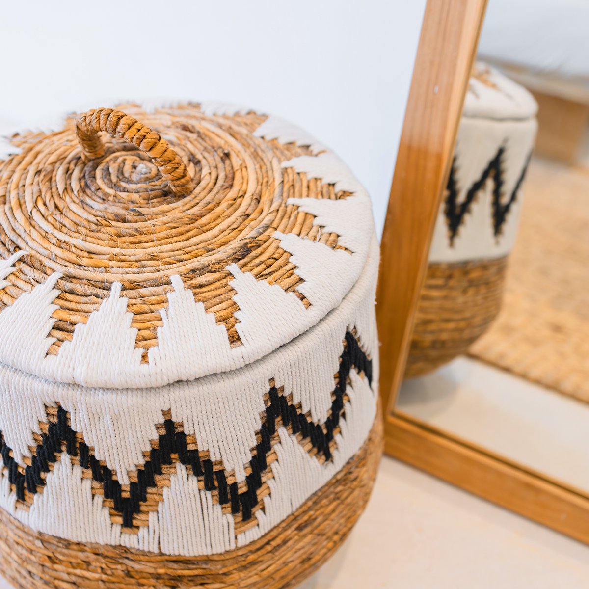 Großer runder Wäschekorb mit Deckel im Boho-Stil, handgeflochten mit dekorativem Baumwollmuster – Modell PAL, ideal zur stilvollen Aufbewahrung ,dekoriert vor einem bodentiefen Spiegel mit Holzrahmen.