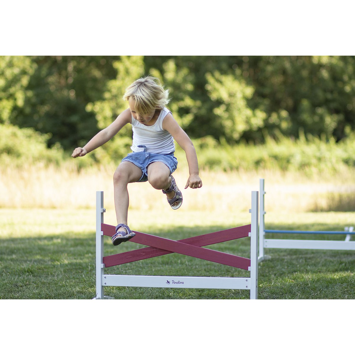 Kind springt über eines der Hürden aus Hürden-Set 'Jumper', 3-teilige, höhenverstellbare Holz-Hürden für motorische Übungen und spielerisches Training.