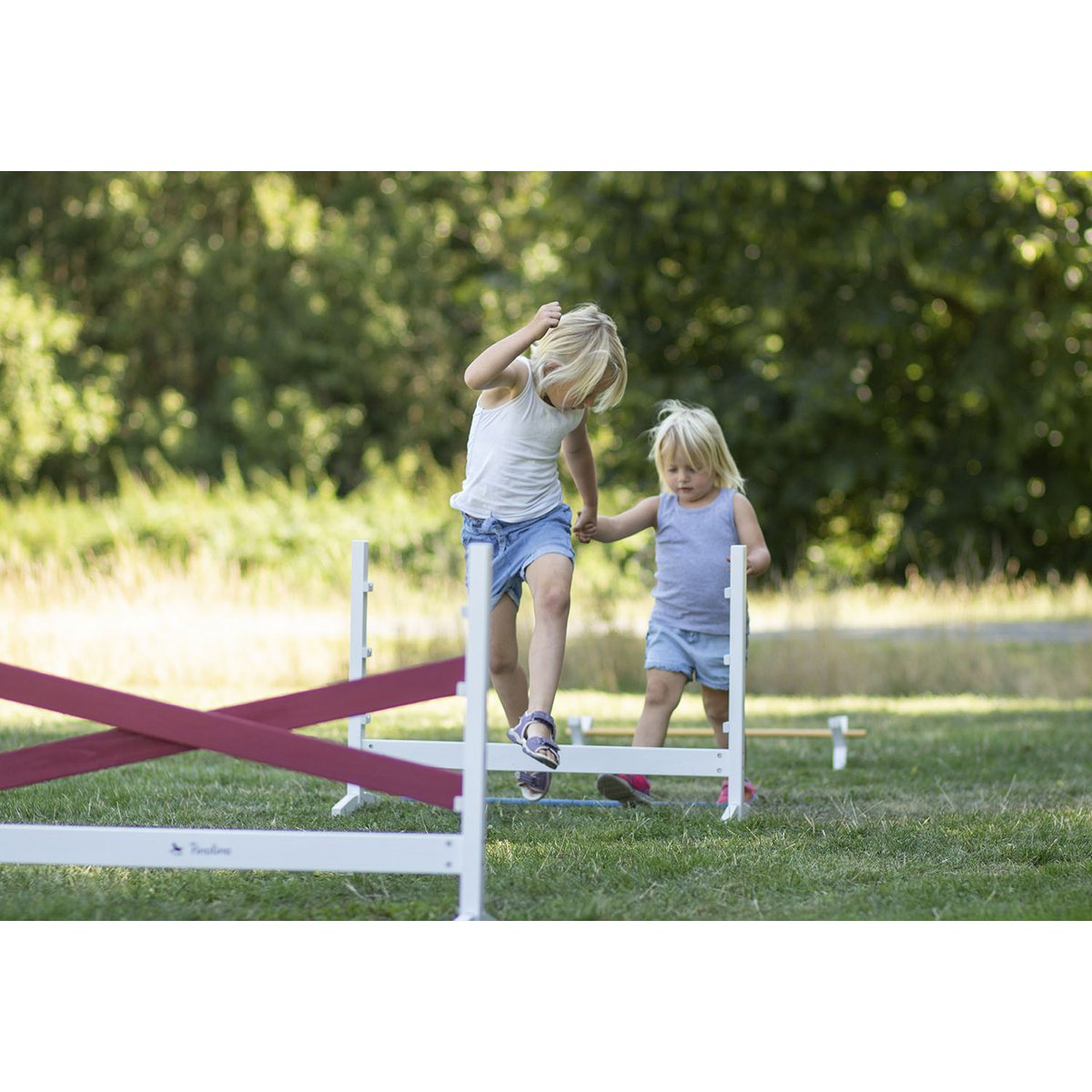 Kinder üben das Springen über Hürden-Set 'Jumper', 3-teilige, höhenverstellbare Holz-Hürden für motorische Übungen und spielerisches Training.
