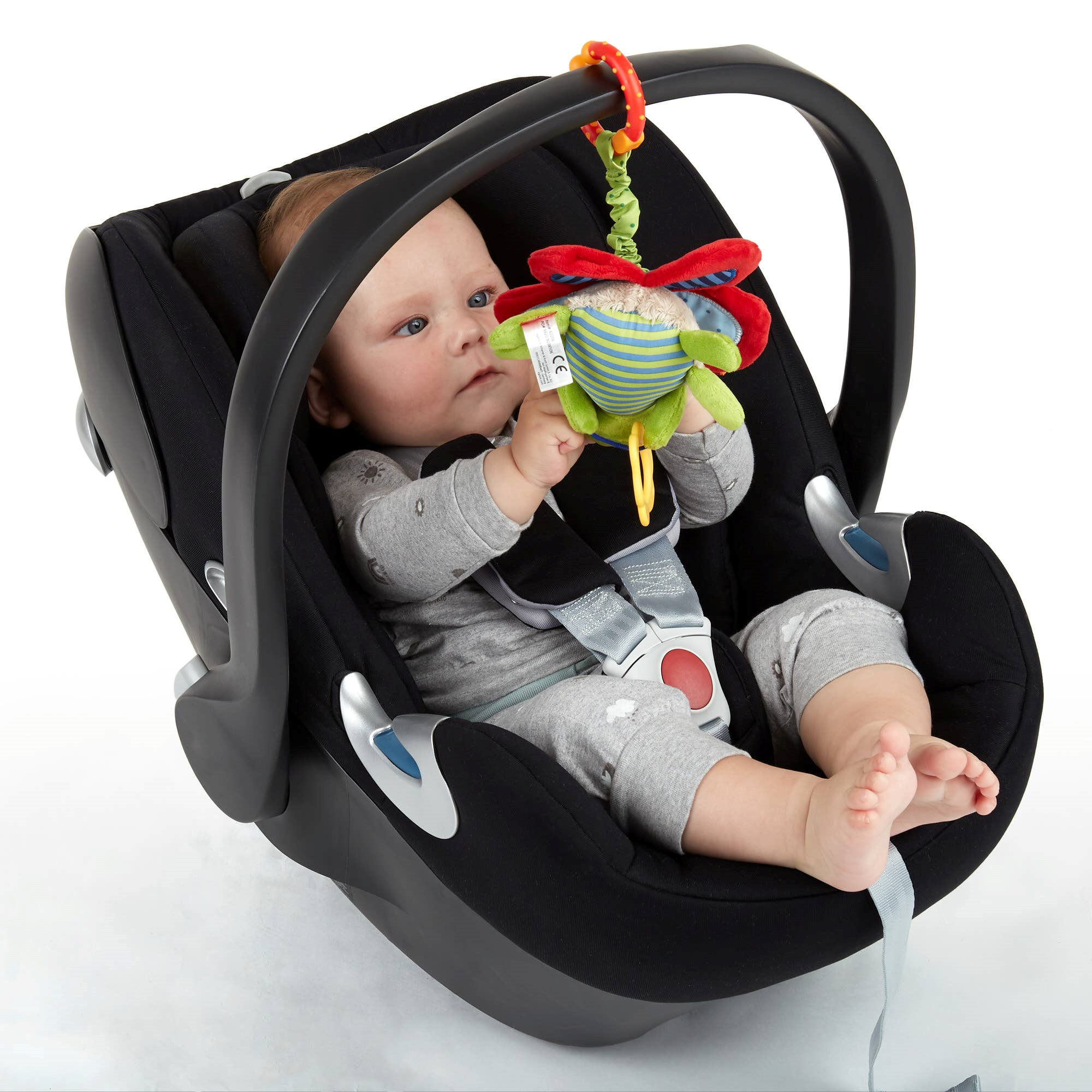 Baby liegt im Maxi Cosi und untersucht Anhänger Schmetterling in Grün und Rot, mit Rassel und Beißring, für Babyschale oder Kinderwagen.