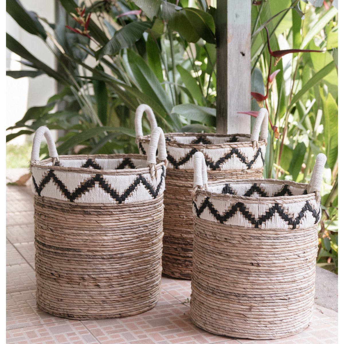 „Korb DALU aus natürlicher Bananenfaser, handgeflochten im Boho-Stil, vielseitig einsetzbar als Wäschekorb, Aufbewahrung oder Pflanzkorb – erhältlich in drei Größen. Der obere Rand ziert ein zickzack Muster in beige und dunkelbraun.