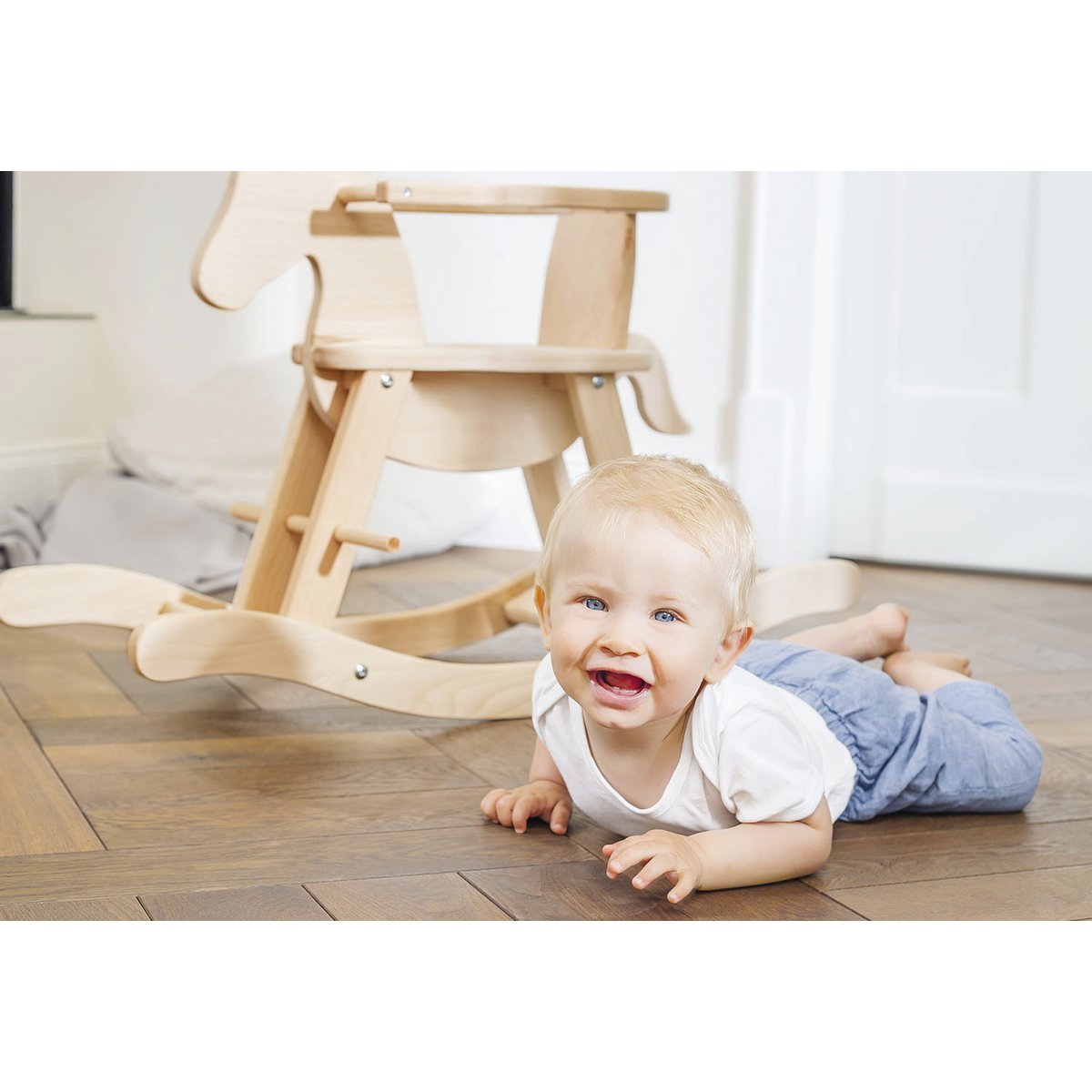 Kind liegt vor dem Schaukelpferd 'Pinolino' aus Holz mit Sicherheitsring, naturfarben, ideal für kleine Kinder ab 1 Jahr.